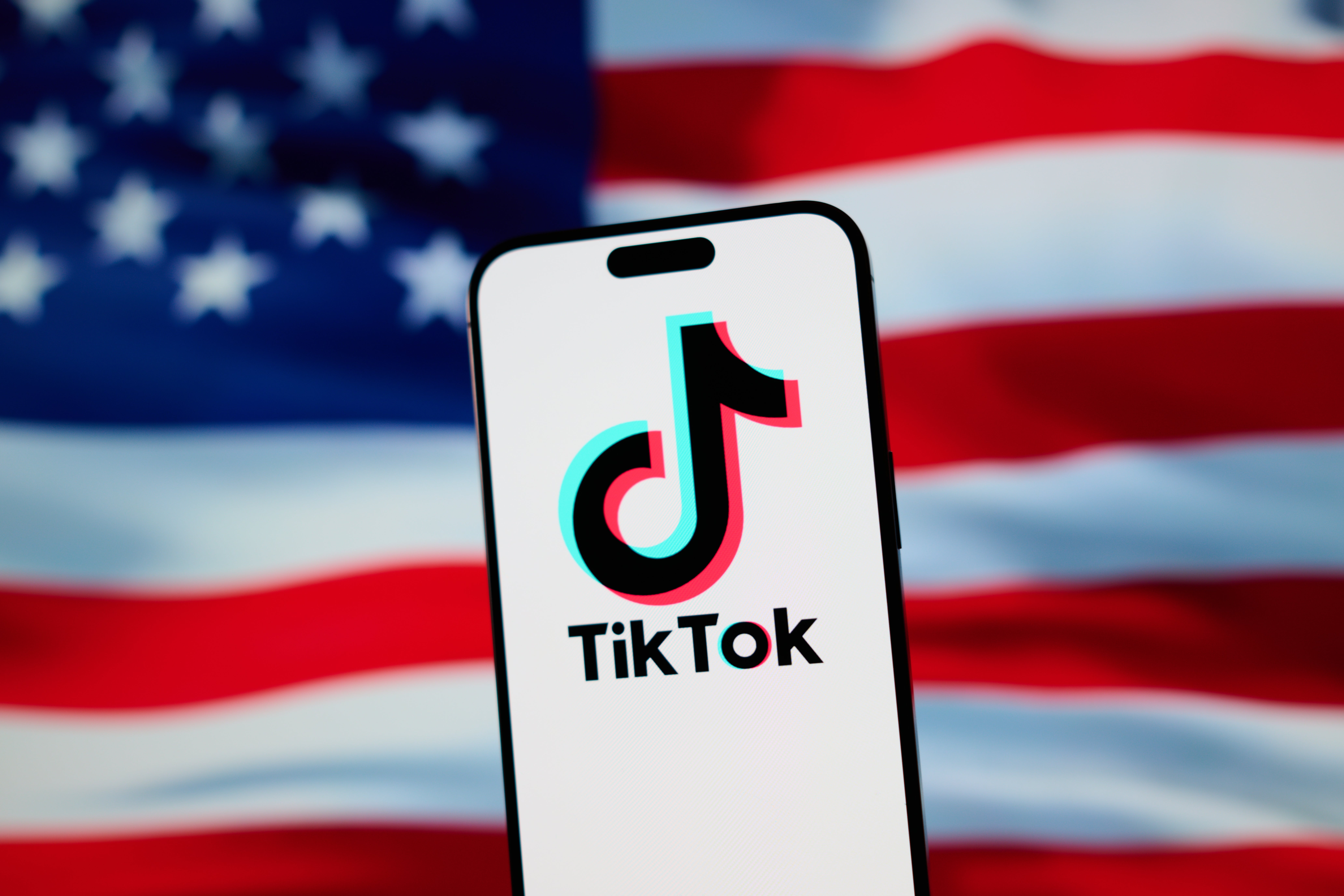 Ilustracja przedstawiająca logo TikTok wyświetlane na telefonie komórkowym nad amerykańską flagą